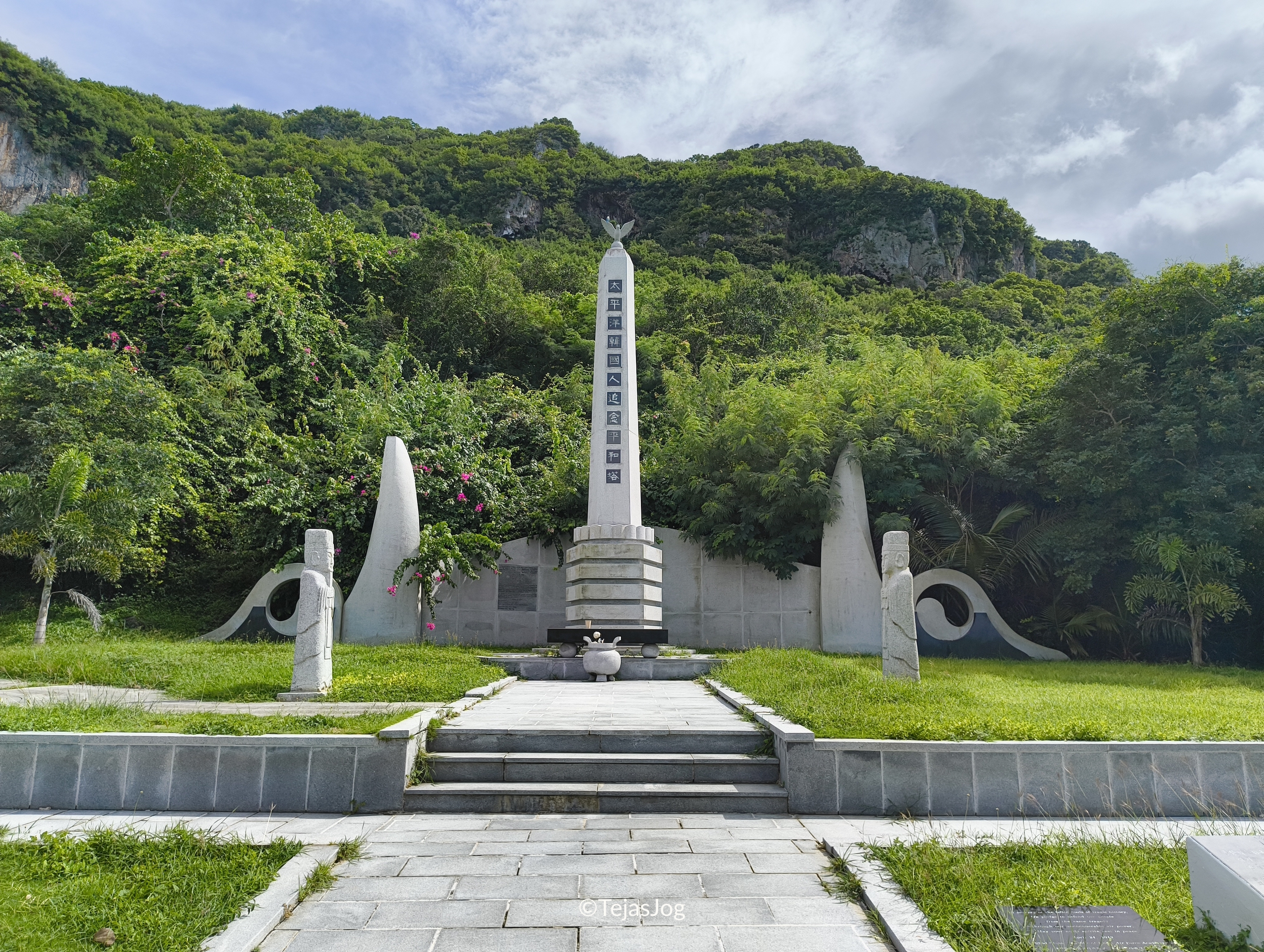 The central monument is a tall, white stone pillar topped with a sculpture of a golden dove or phoenix, symbolizing the flight of the soul toward peace
