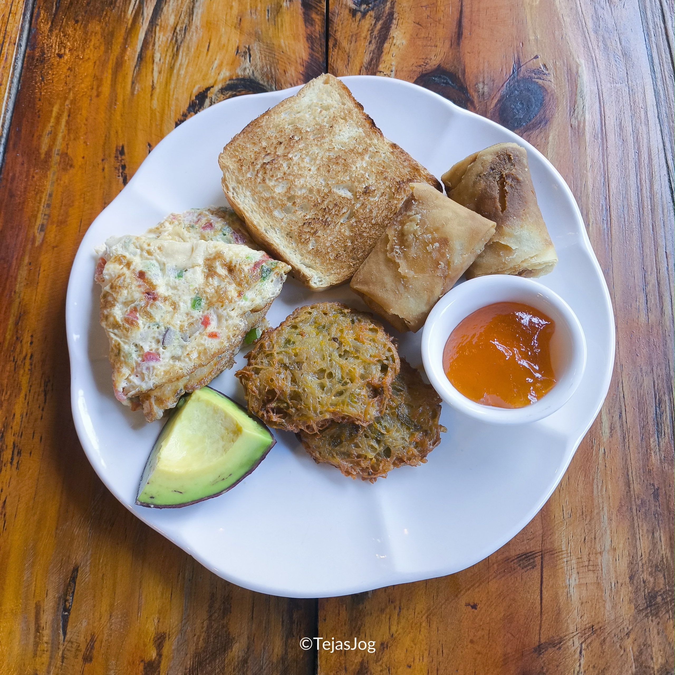 Omelet with vegetables, potato pancakes, a roll with white cheese, toast with butter and jam, and avocado
